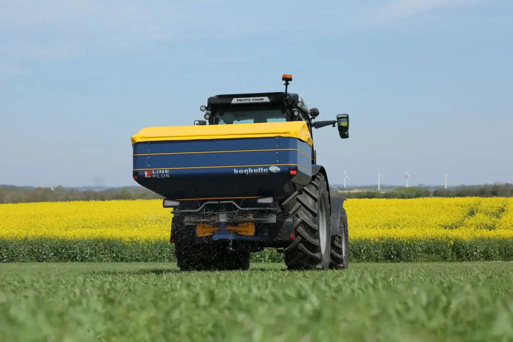 Vista trasera de la abonadora Bogballe L15W plus junto a un campo de colza en flor
