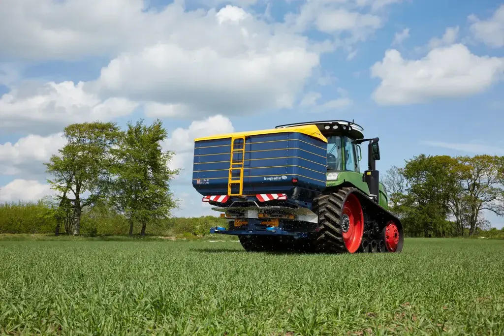 Abonadora Bogballe M60W plus enganchada a un tractor de orugas en el campo